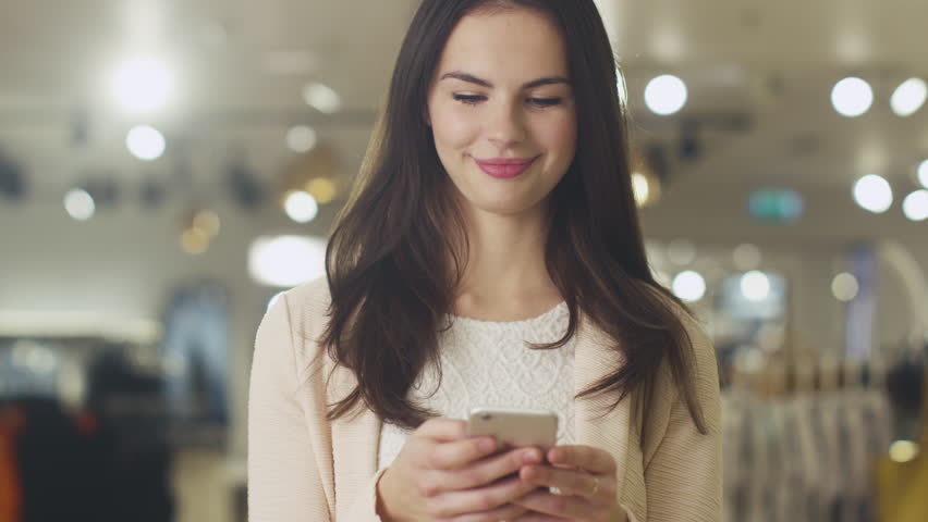 Happy Young Brunette Girl Is Standing In A Department Store And Texting 