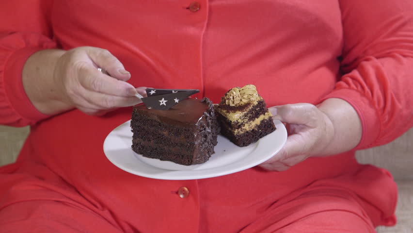 Overweight Mature Woman Sitting On A Couch And Eating Cake Stock