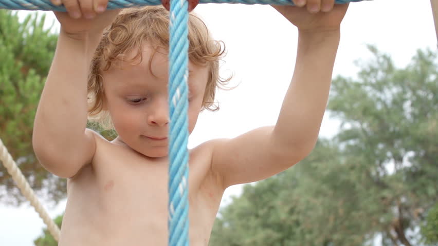 Slow Motion Close Shot Of A Cute Young Boy Climbing Up A Rope Ladder In