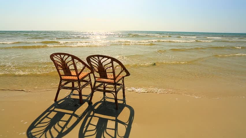 Sunset On A Beach. Two Empty Wooden Chairs Standing In A Water. Stock 