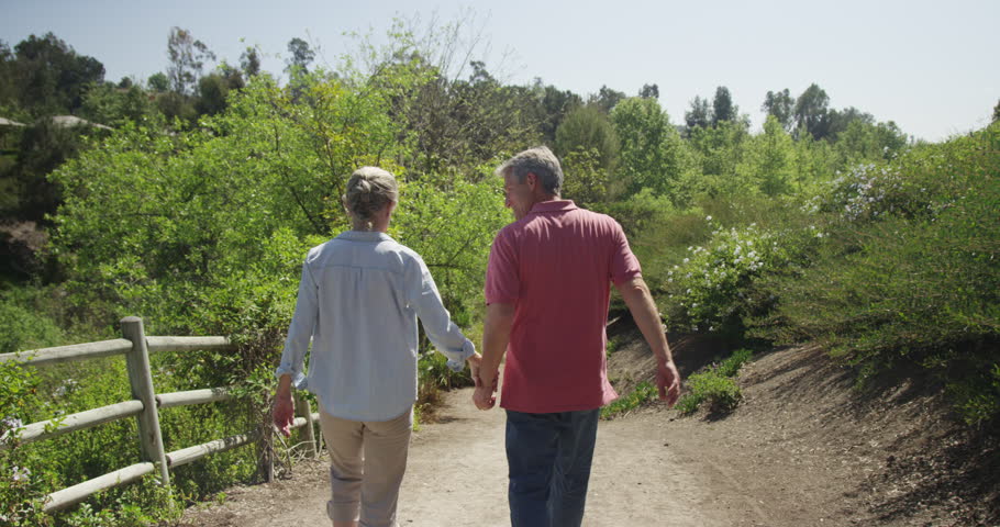 Couple Holding Hands Walk On Nature Trail. Mature Couple Walking Along