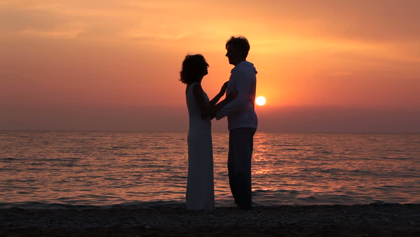 Romantic Couple Is Enjoying Sunset Sitting On The Beach And Hugging ...