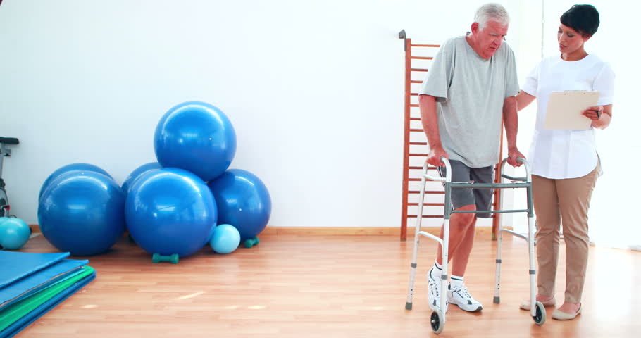 Smiling Physiotherapist Helping Patient Walk With Zimmer Frame At The ...